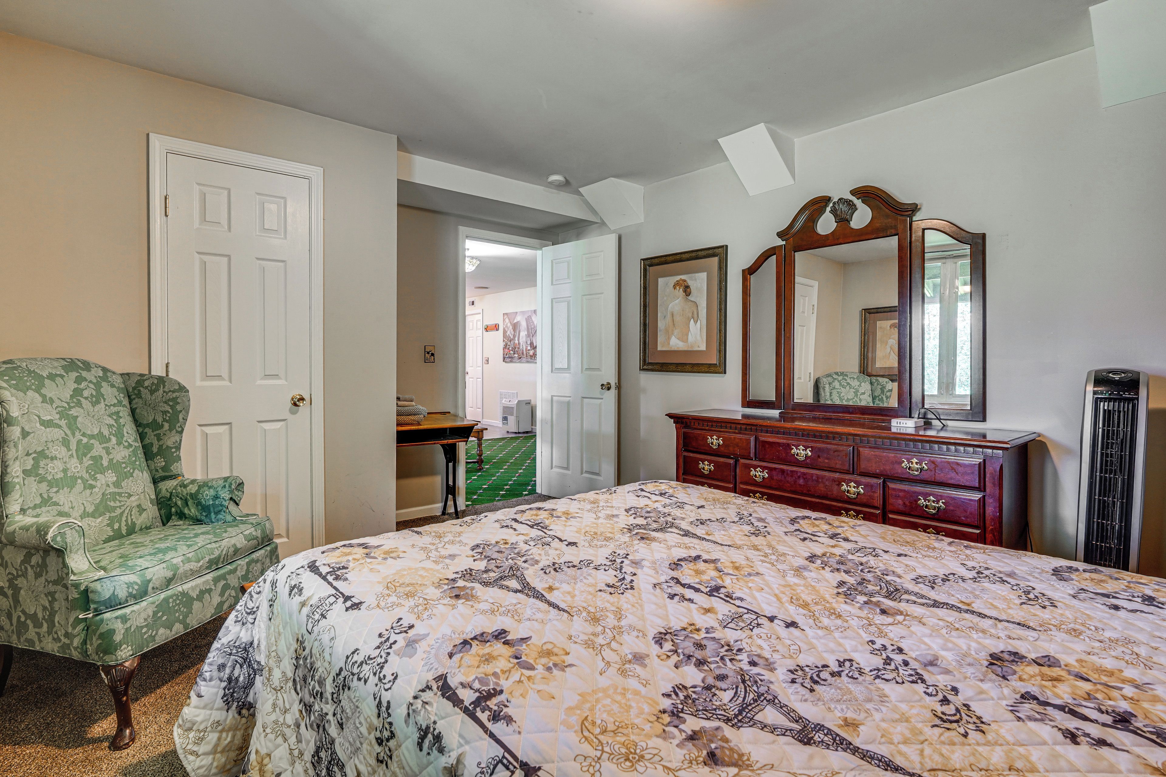 Un dormitorio con cama, cómoda, silla y una puerta que da a otra habitación.