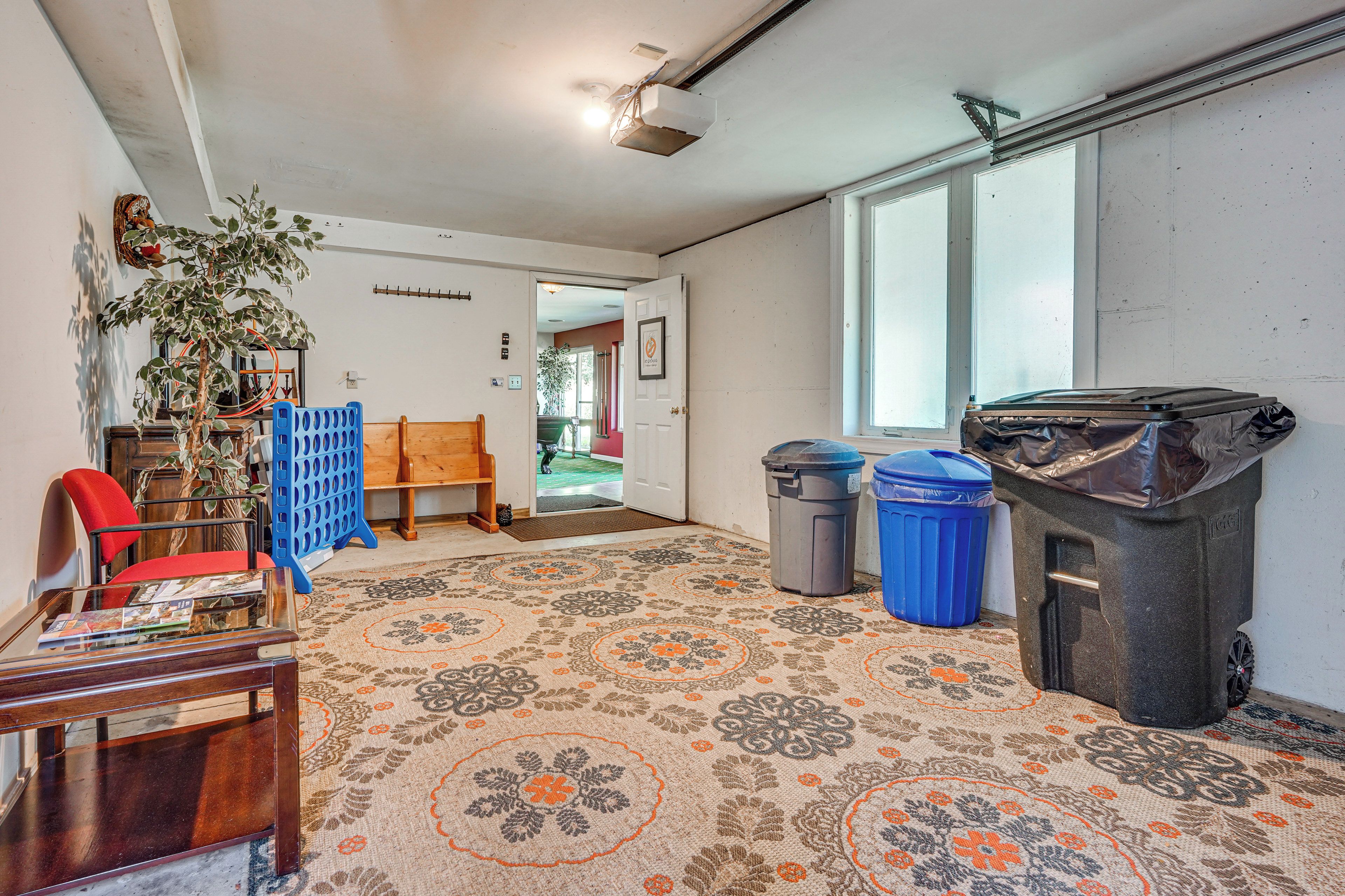 A room with a patterned carpet, a wooden chair, a red chair, a table with magazines, a plant, and two trash bins.