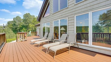 A deck with sun loungers and a view of a forested area.