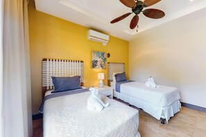A hotel room with two beds, a ceiling fan, an air conditioning unit, and a decorative wall piece. - Ocean-view Ocotal Villa, Balcony & Pool (Sardinal)