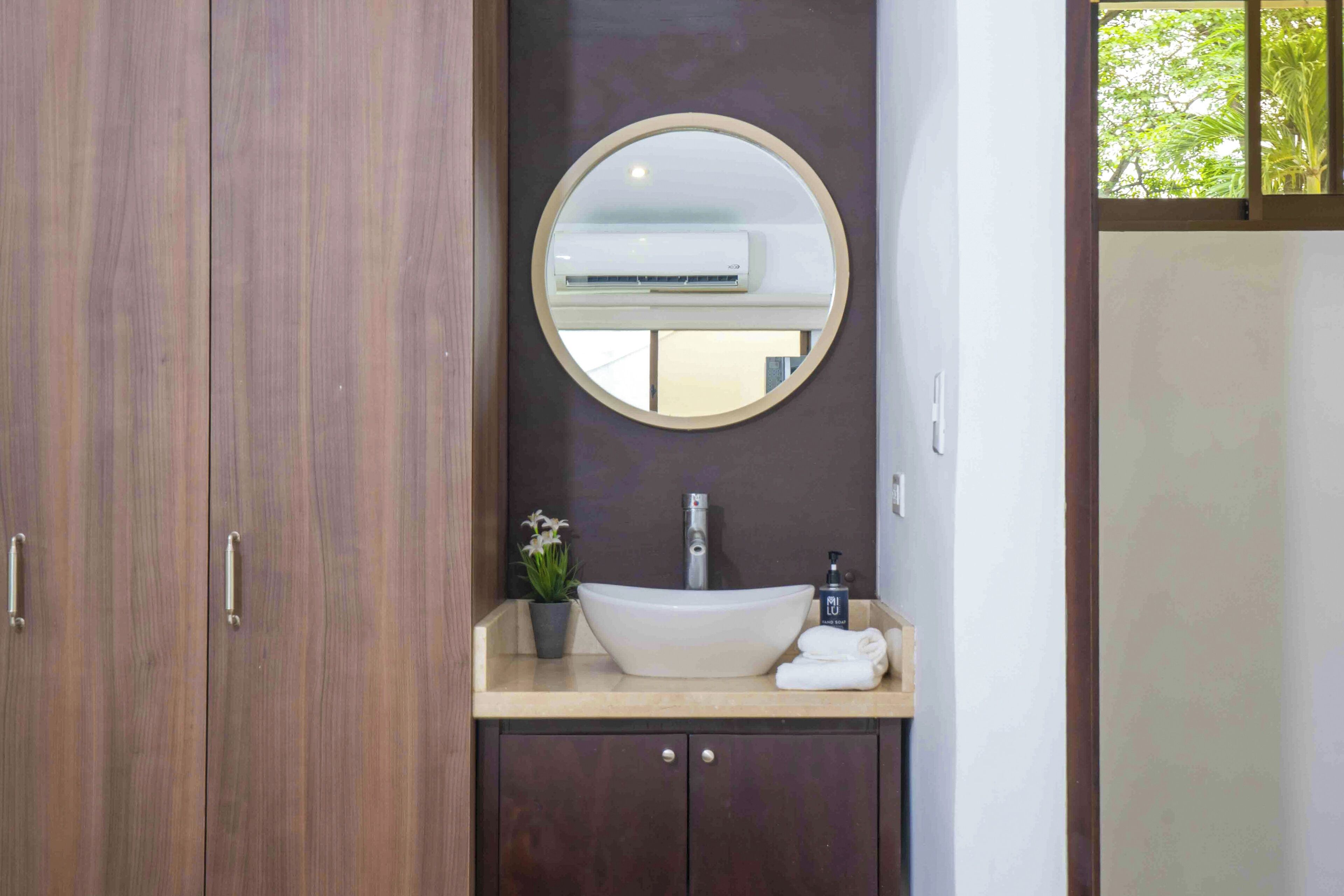 A bathroom with a round mirror, a sink, a potted plant, and a towel.