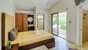 Habitación de hotel con cama, baño, televisor y puerta corrediza de vidrio al exterior.