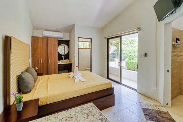 A hotel room with a bed, a bathroom, a TV, and a sliding glass door to the outside.