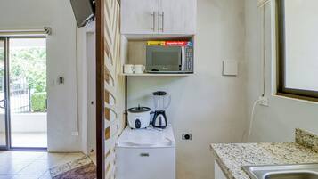 Una kitchenette compacta con microondas, licuadora y refrigerador pequeño.