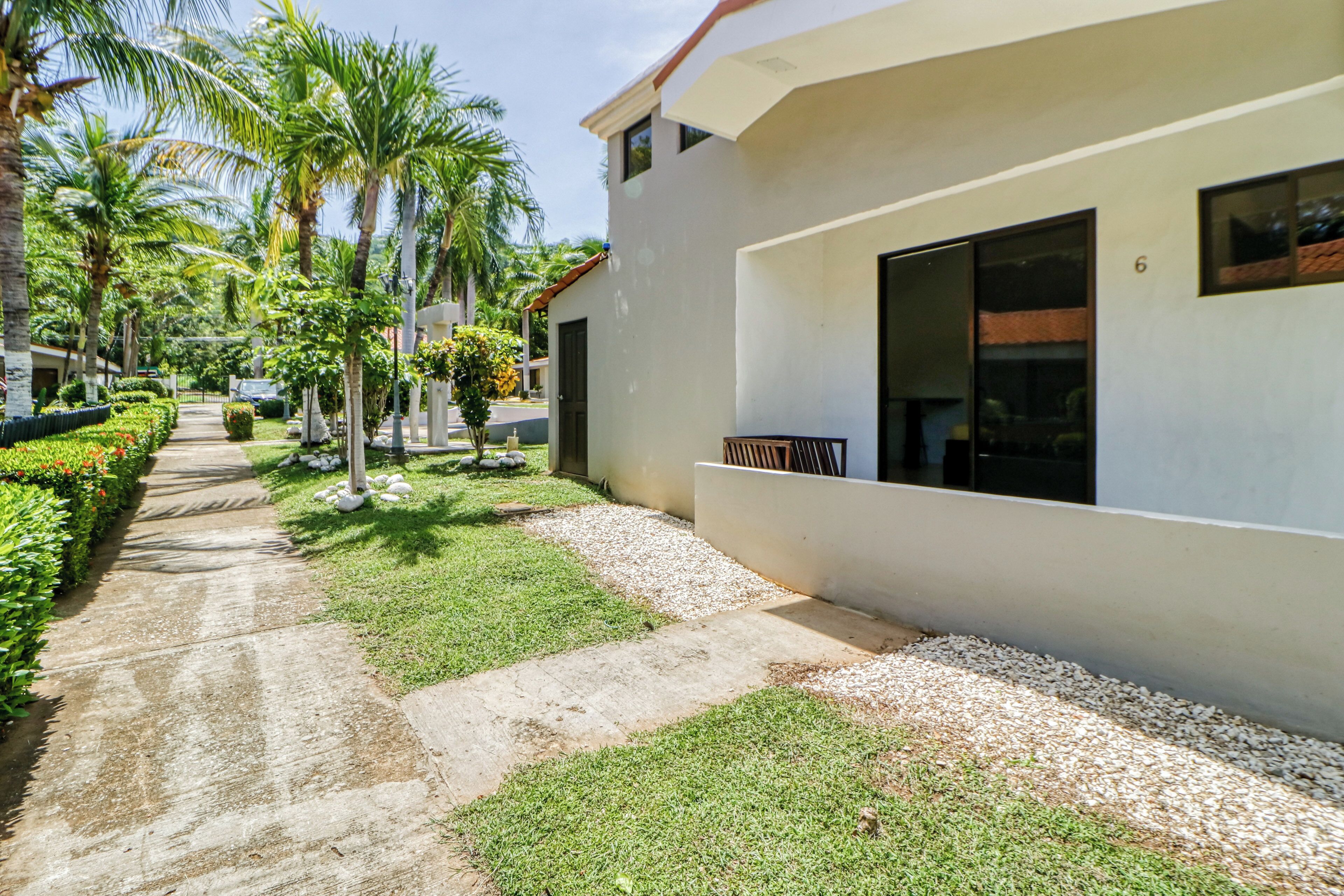 A modern building with a paved walkway, palm trees, and a well-maintained lawn.