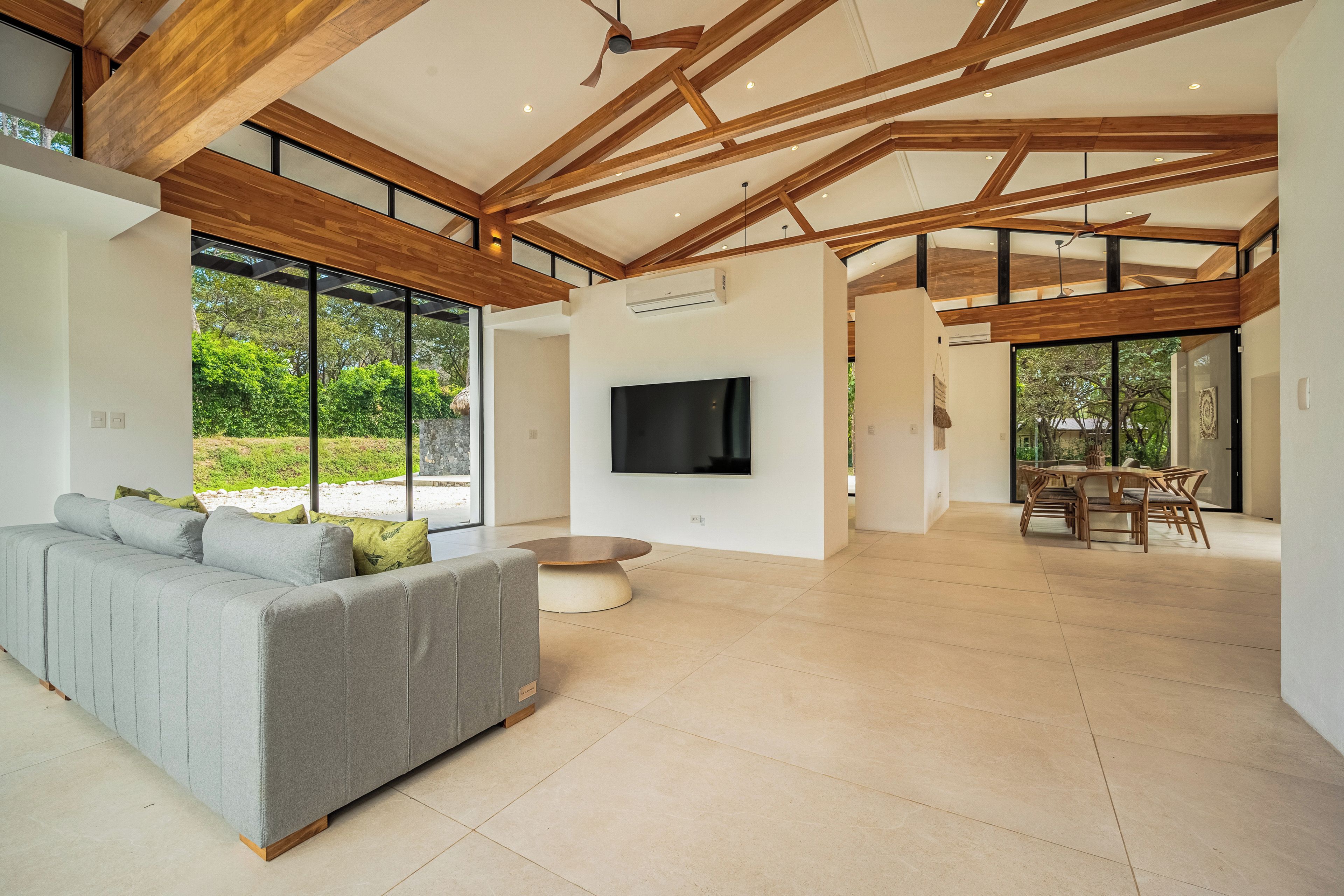 A spacious living area with a grey sofa, a flat-screen TV, and a dining area with wooden furniture.