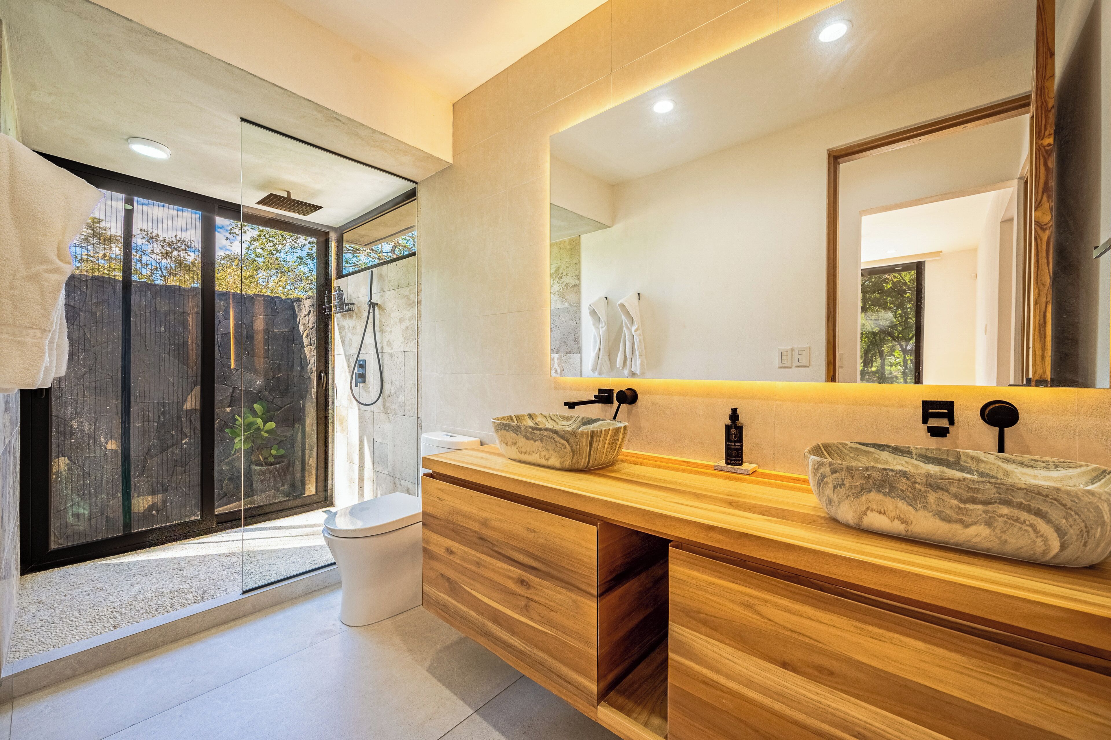 Un bagno moderno con un ampio specchio, un mobile vanitario in legno e una zona doccia.