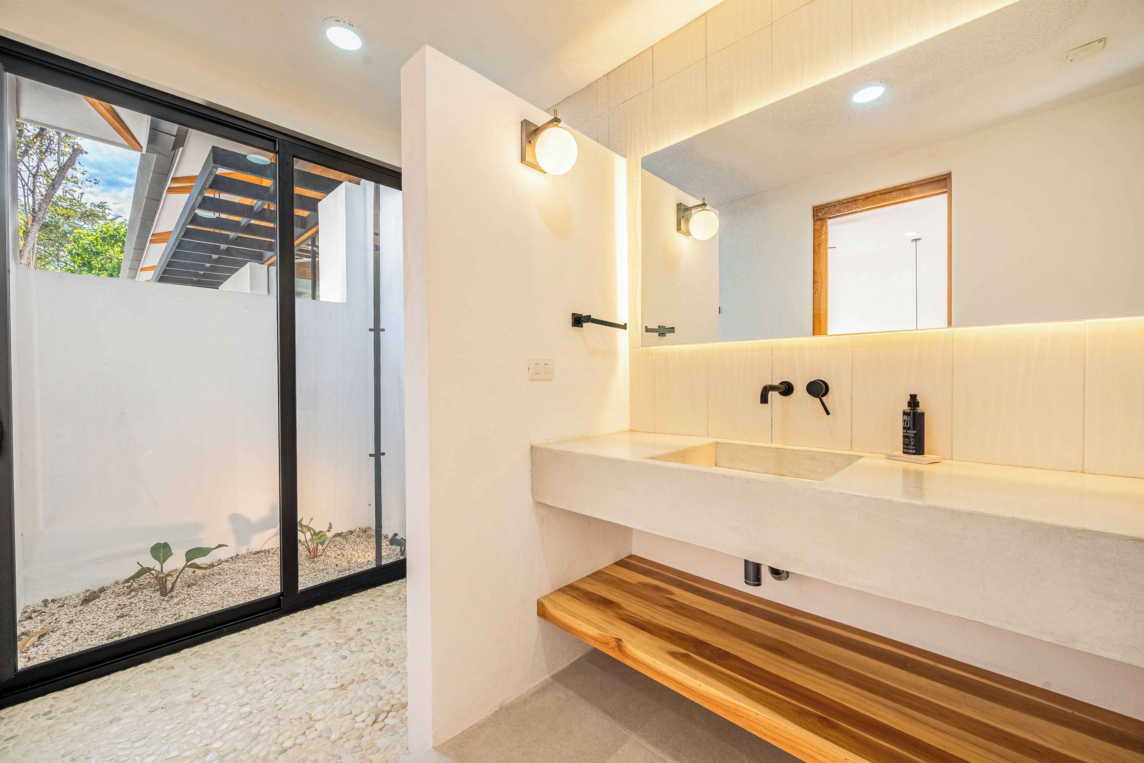 Un baño moderno con un espejo grande, dos lavamanos y un banco de madera.