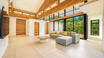 A spacious living area with a modern design, featuring a large window, a sofa set, and a coffee table.