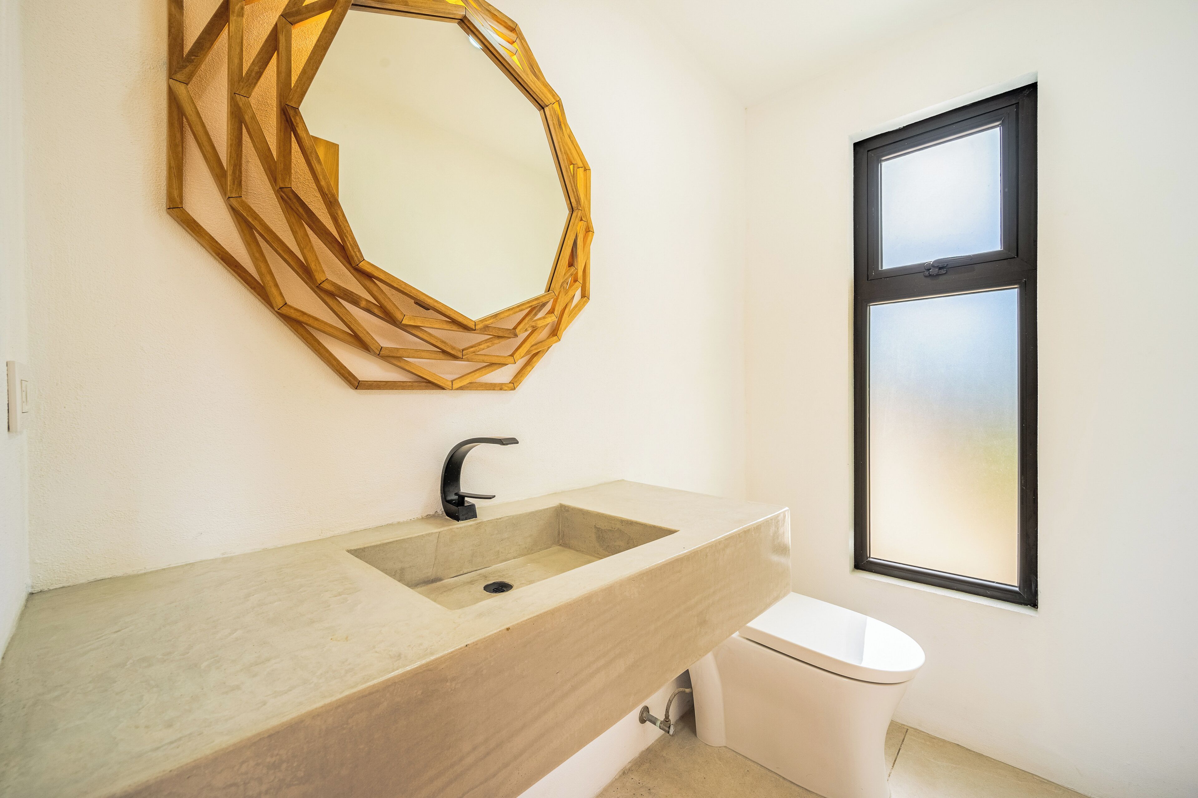 A bathroom with a large, geometric mirror, a sink with a modern faucet, and a toilet.