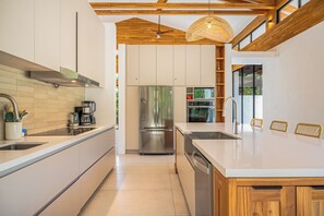 Een moderne keuken met een centraal eiland, roestvrijstalen apparatuur en een houten plafond.