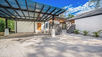 A modern house with a covered patio, stone walls, and a gravel driveway.