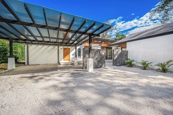 A modern house with a covered patio, stone walls, and a gravel driveway. - Walk to 2 Beaches! Villa w/ Pool, Lava-stone Spa (Cabo Velas)
