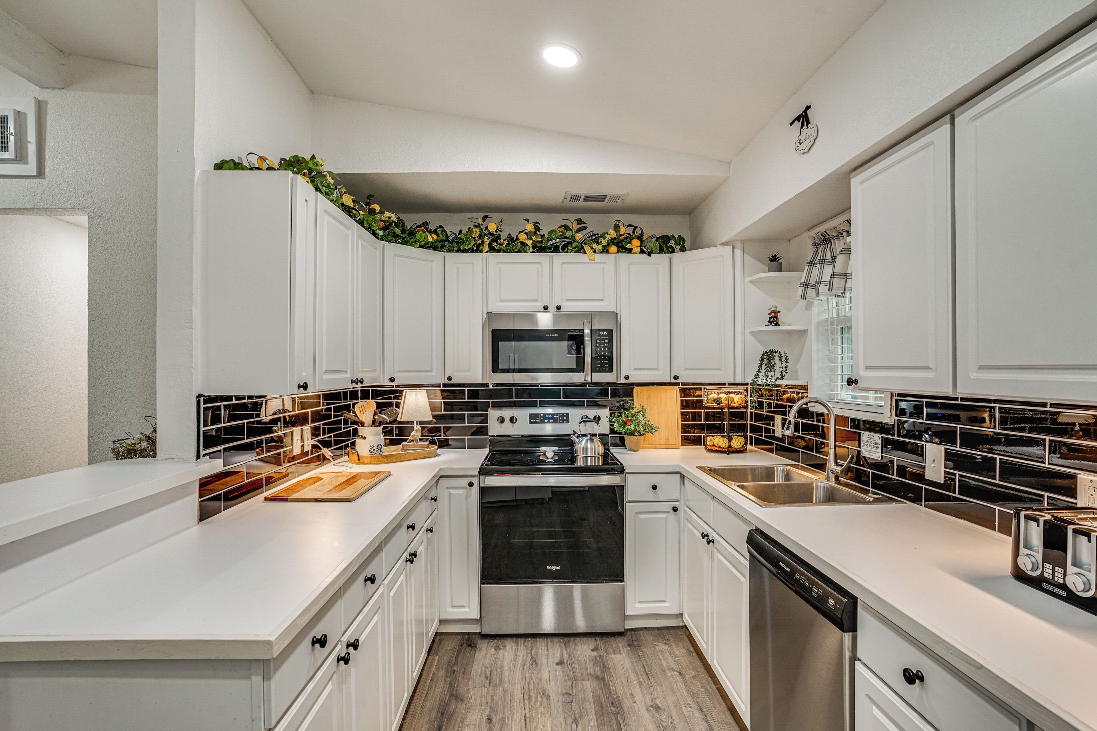 A modern kitchen with white cabinetry, stainless steel appliances, and a black backsplash.