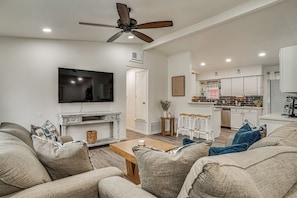 A modern living room with a flat-screen TV, a ceiling fan, and a kitchen area with white cabinets and a built-in oven. - Explore Arlington! Centrally Located Extended Stay (Arlington)