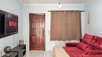A living room with a red sofa, a television mounted on the wall, a wooden door, and a curtain.