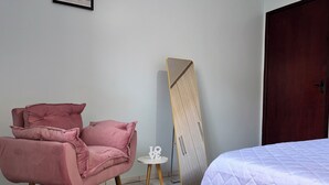 A bedroom with a bed, a pink chair, a small white table, and a wardrobe.
