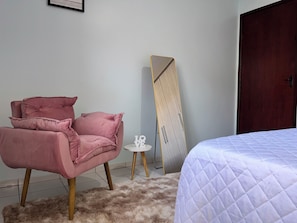 Una camera da letto con un letto, una poltrona rosa, un piccolo tavolo bianco e un armadio.