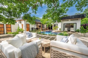 A modern outdoor living area with a pool, white furniture, and a covered patio. - Modern Tamarindo Villa Private Pool & Garden (Tamarindo)