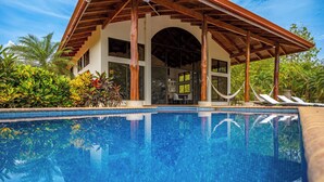 A pool area with a covered seating area, a view of the pool, and surrounding greenery. - Luxe Ocean-view Hideaway in Carrillo (Puerto Carrillo)