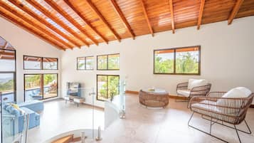 A spacious living area with a high ceiling, large windows, and a pool view.