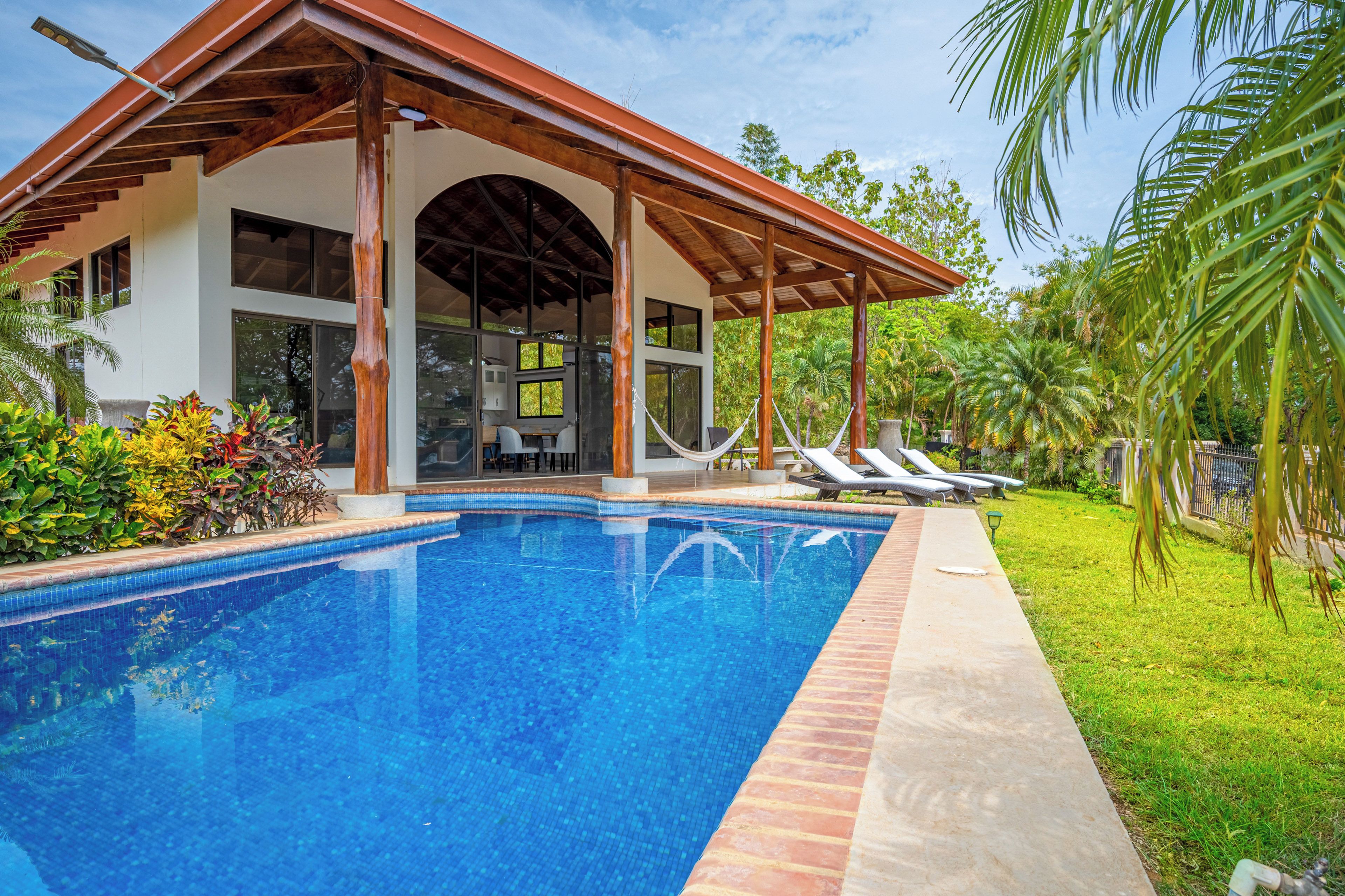 A modern house with a swimming pool, a covered patio, and a lush garden.