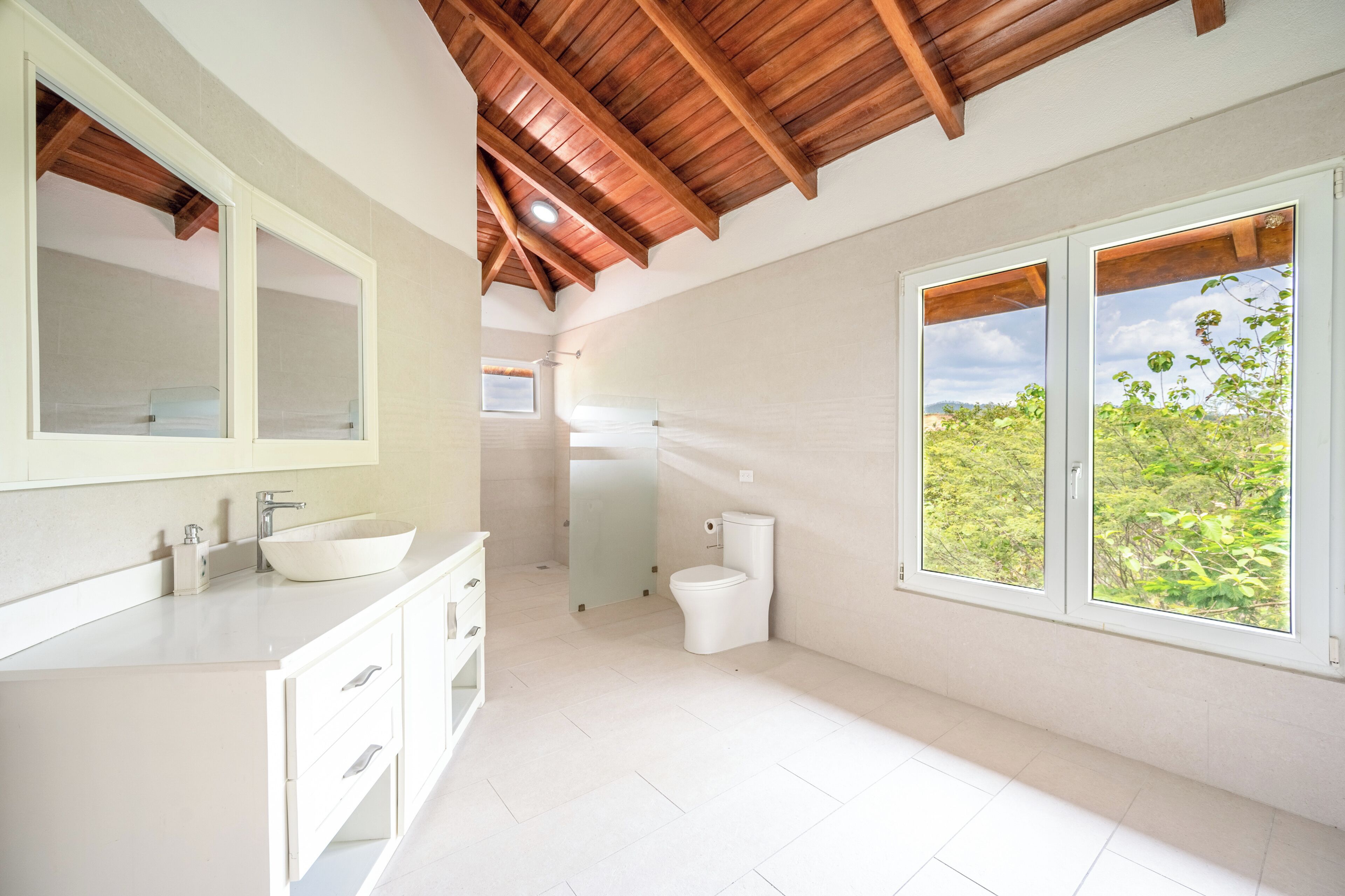 Une salle de bain moderne avec une grande fenêtre, un plafond en bois et un lavabo blanc.