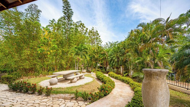 A garden with a stone pathway, a central seating area with benches, and a large stone planter. - Luxe Ocean-view Hideaway in Carrillo (Puerto Carrillo)