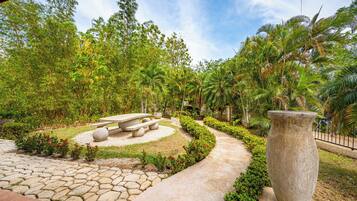A garden with a stone pathway, a central seating area with benches, and a large stone planter.