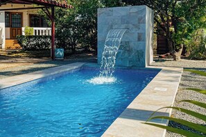 A swimming pool with a waterfall feature, surrounded by a stone wall and a covered area with steps leading to a door. - Santa Cruz Group Getaway w/ Pool: Walk to Beach (Veintisiete de Abril)