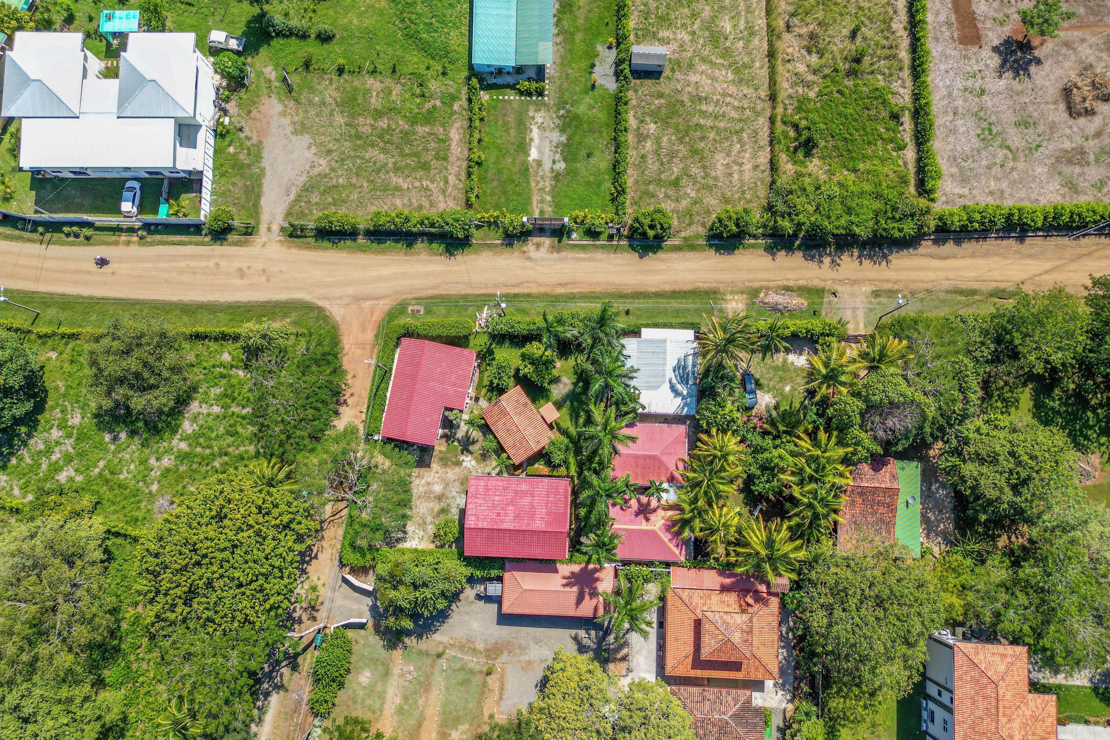 An aerial view of a residential area with multiple houses, a dirt road, and surrounding greenery.