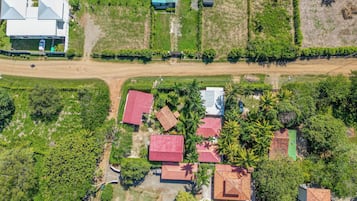 An aerial view of a residential area with multiple houses, a dirt road, and surrounding greenery.