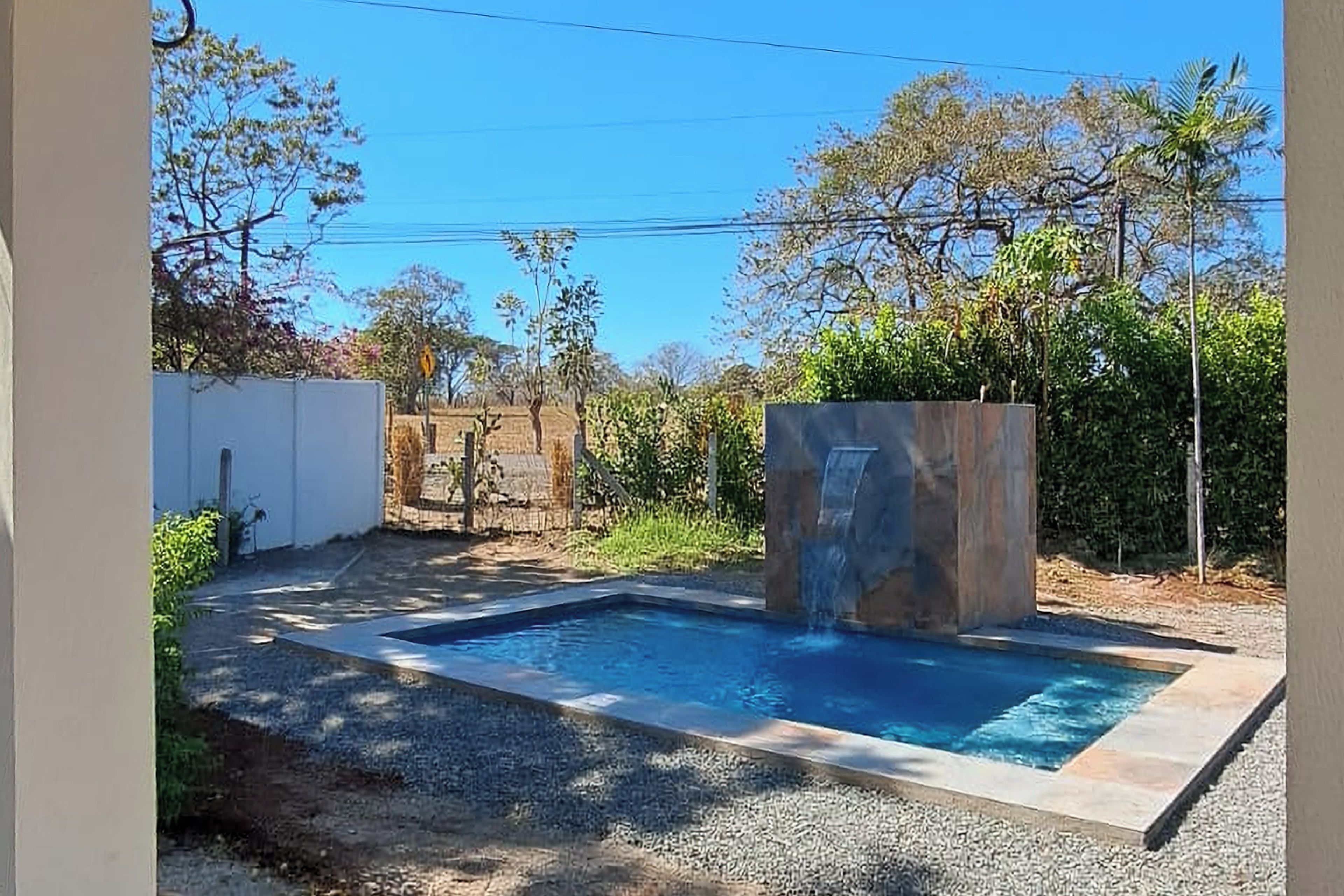 Una piscina rectangular amb cascada, envoltada per una paret blanca i vegetació.