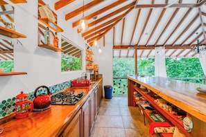 A kitchen with wooden beams, a gas stove, a red kettle, and a view of greenery outside. - Secluded Ojochal Studio w/ Trails & Pool Access! (Ciudad Cortés)