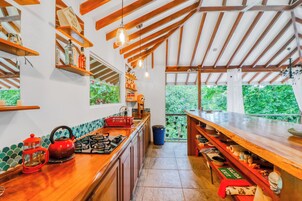 Cocina con vigas de madera, cocina a gas, hervidor rojo y vistas a zonas verdes.