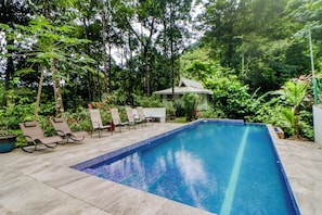 A rectangular pool with tiled edges, surrounded by lounge chairs and potted plants, with a building in the background. - Secluded Ojochal Studio w/ Trails & Pool Access! (Ciudad Cortés)