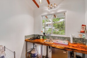 A compact kitchen with a wooden countertop, a gas stove, a sink, and a window overlooking a lush garden. - Secluded Ojochal Studio w/ Trails & Pool Access! (Ciudad Cortés)