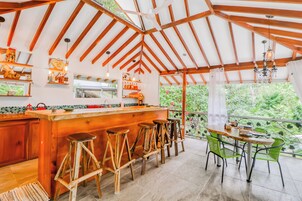 Una cocina con taburetes de madera, una mesa de comedor con sillas y vistas a la vegetación por la ventana.