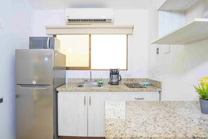 Eine kompakte Küche mit integriertem Mikrowellenherd, Kühlschrank, Kaffeemaschine und einem Fenster über der Spüle.