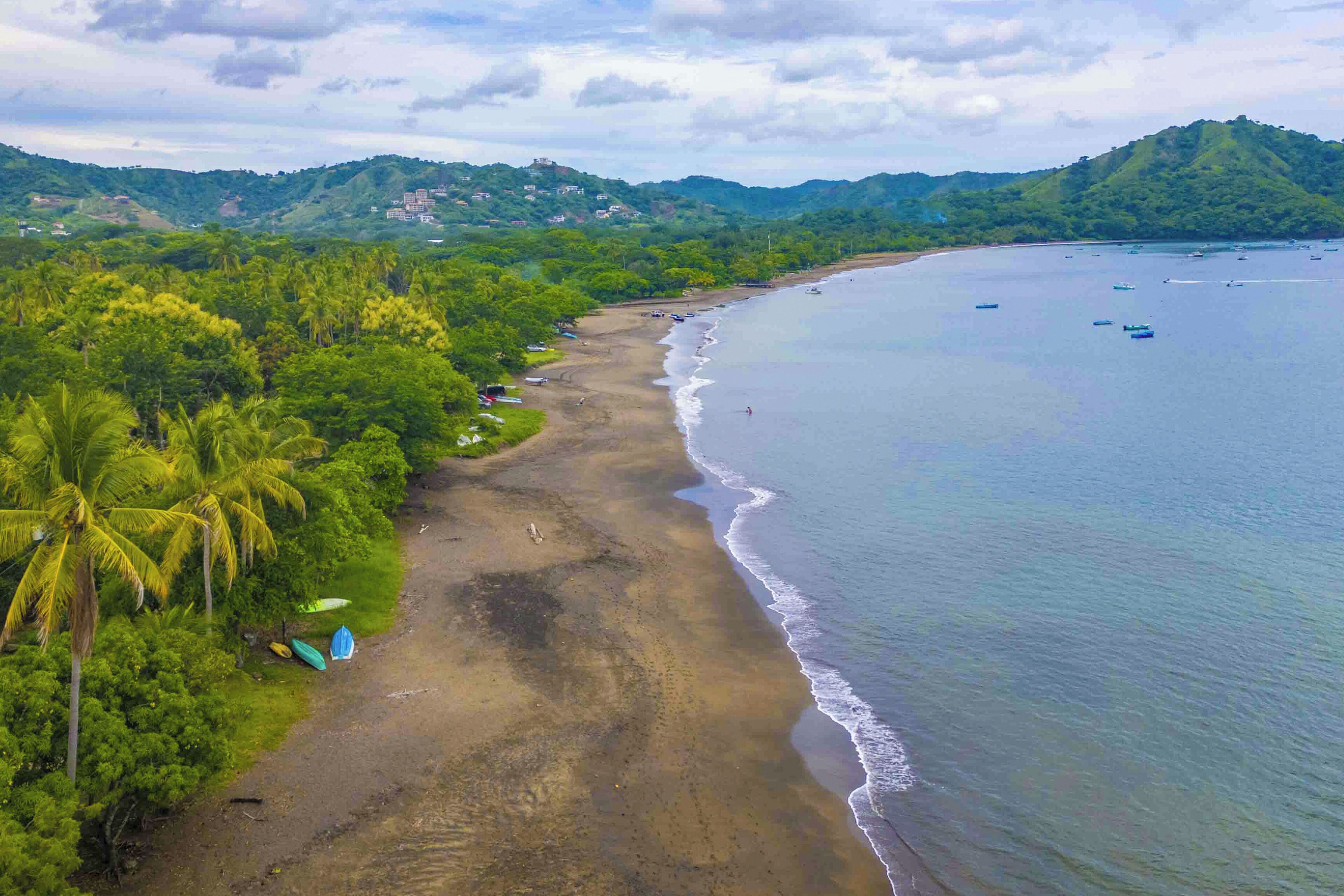 A beach with a clear view of the ocean and a forested hillside in the background.