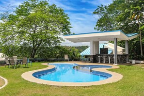 A swimming pool with a covered area, surrounded by grass and trees.