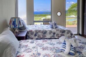 A bedroom with two beds, a lamp, and a view of a pool and greenery.
