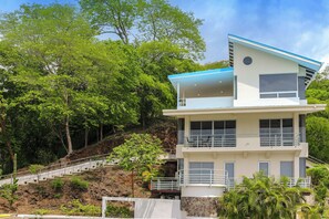 A multi-story building with a balcony on the upper level, surrounded by lush greenery.