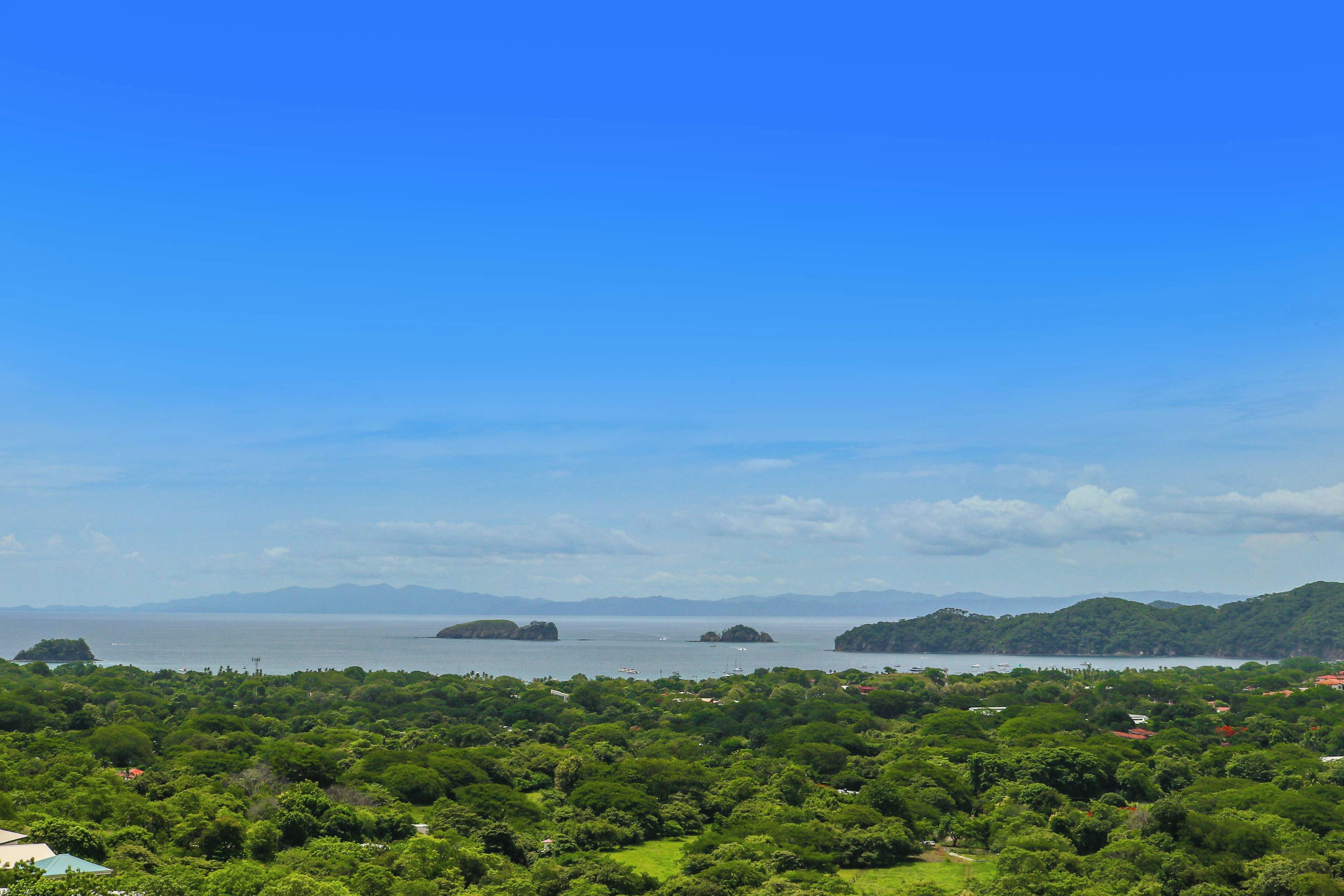 Un paysage côtier caractérisé par une végétation luxuriante, un ciel dégagé et des îles lointaines.