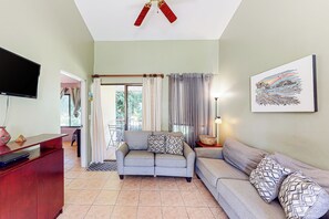 A living room with a grey sofa, a television, and a painting on the wall. - Playa Ocotal Condo w/ Pool: Walk to the Beach! (Sardinal)