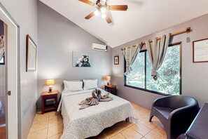 A hotel room with a bed, two bedside tables with lamps, a ceiling fan, a window with curtains, and a chair. - Playa Ocotal Condo w/ Pool: Walk to the Beach! (Sardinal)