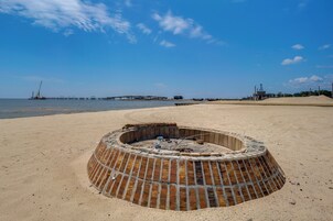 A beach with a circular brick fire pit in the foreground.