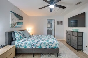 A bedroom with a bed, a desk, a dresser, a ceiling fan, a TV, and a painting on the wall.