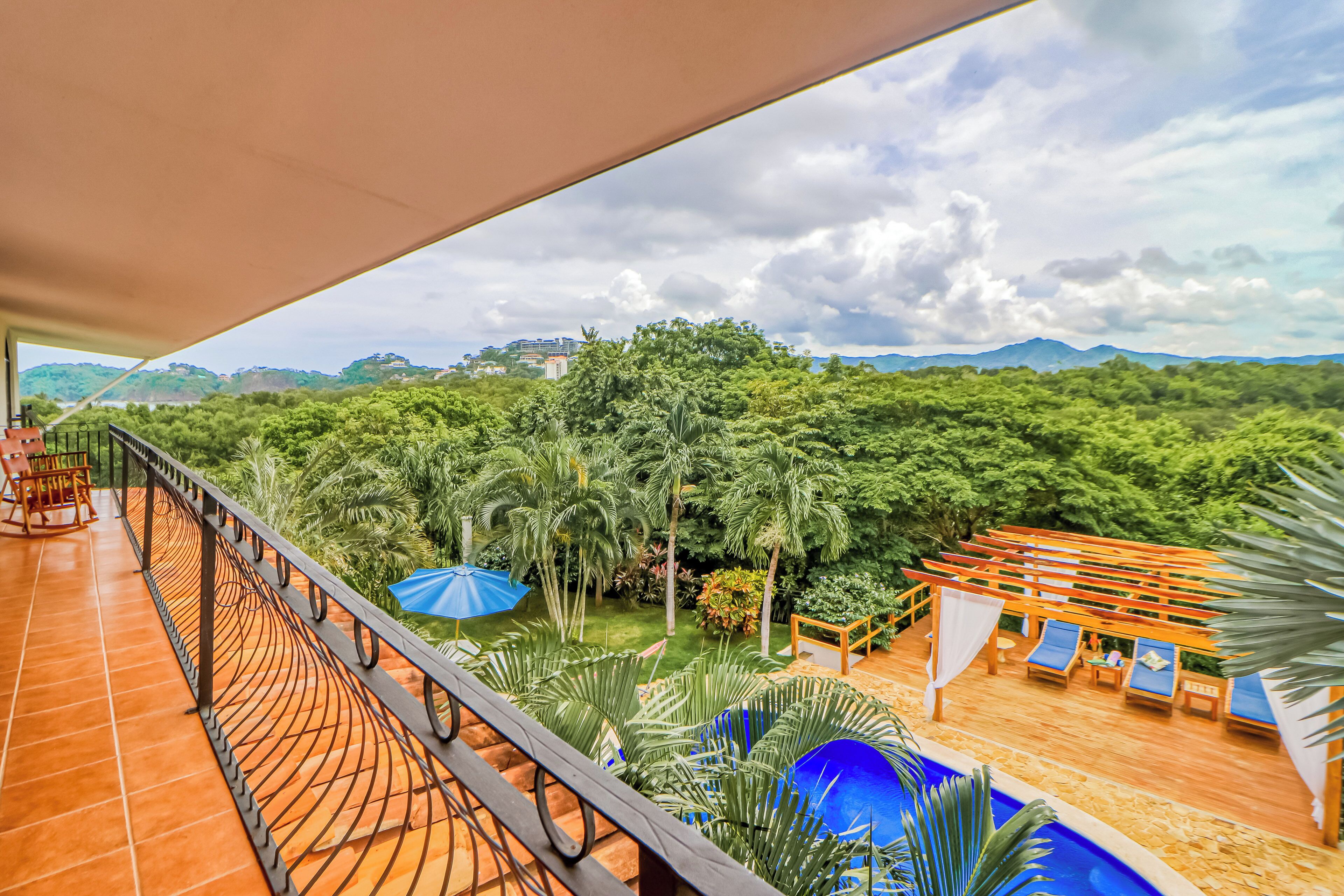 A balcony with a view of a lush garden and distant mountains.