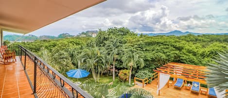 A balcony with a view of a lush garden and distant mountains.